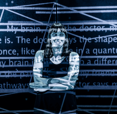 A woman with her arms crossed, with projected shapes, patterns and words appearing over her face and body.