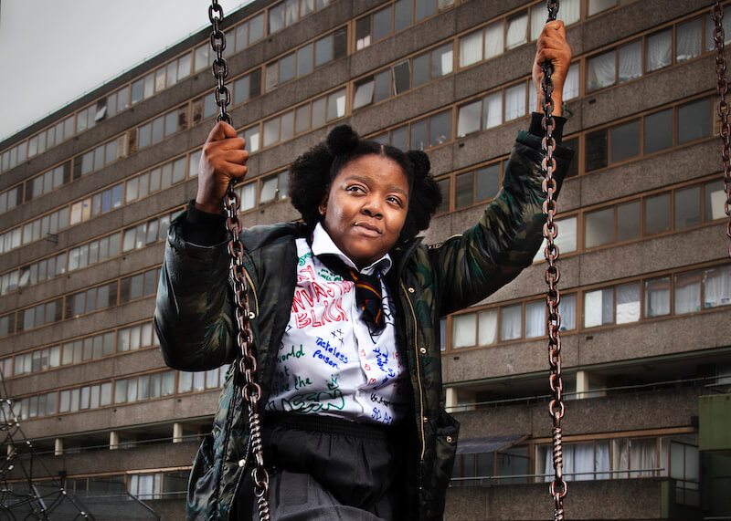 A young woman dressed in a school uniform, holding onto a swing, and looking away from the camera.