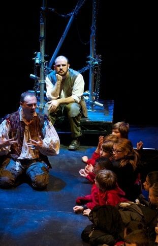 A man kneeling down, dressed in costume, talking to a group of school children.