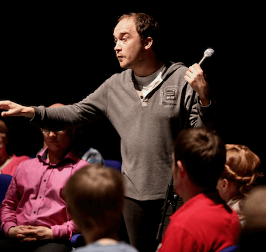 A man amongst an audience with a microphone in his hand.