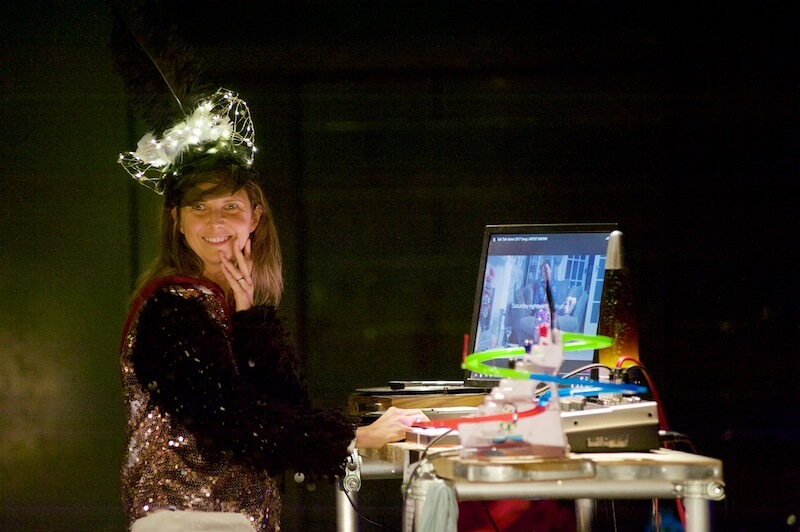 A woman wearing a head dress, standing at a table made of scaffolding, which has a computer screen on top of it.