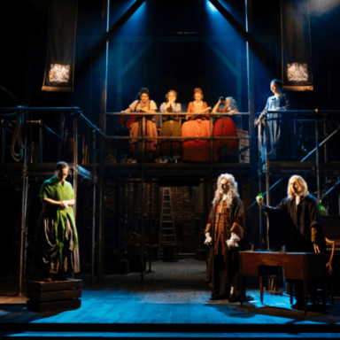 Five women looking down from a scaffolding platform and three other actors on stage.