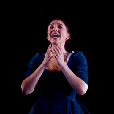 A young woman holding her arms up towards her face whilst she sings.
