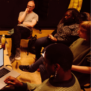 Four people sat round in a semi-circle. They appear to be listening to someone out of shot.