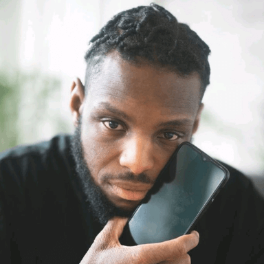 A man looks directly at the camera holding a phone to his face.