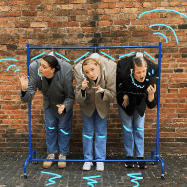Three women inside suit jackets hanging on a clothes rail in front of a brick wall