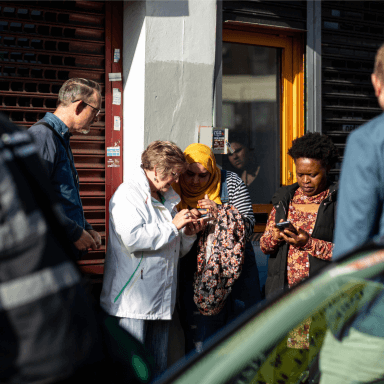 A group of people looking at their phones outside some shop fronts.