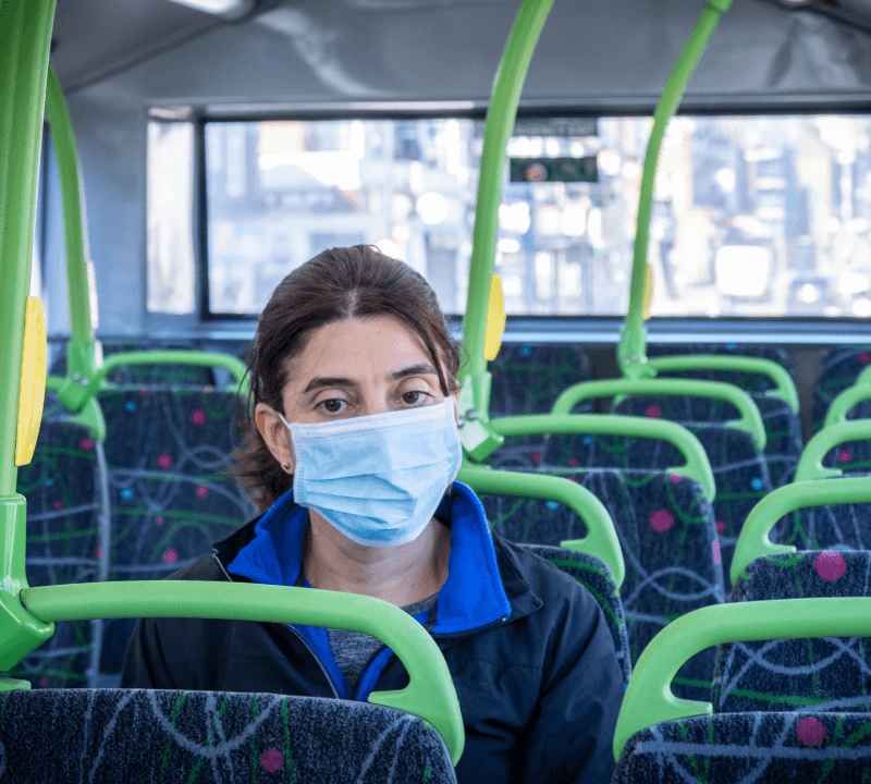A woman wearing a disposable mask, sitting on a bus alone.