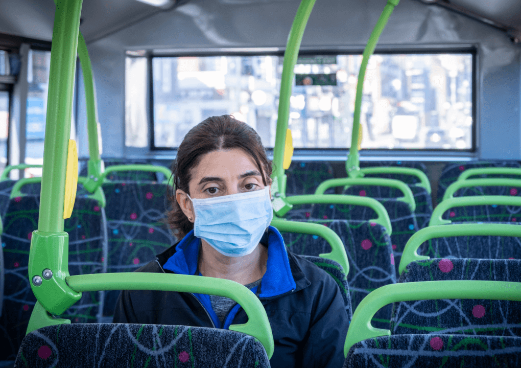 A woman wearing a disposable mask, sitting on a bus alone.