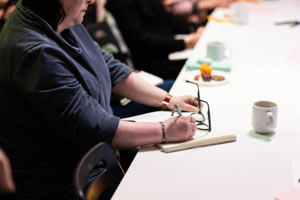 A photograph focusing on a person writing in a notepad.