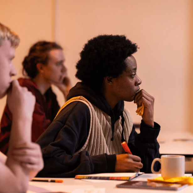 A side profile of three people, each of them is resting their chin on their hand. They appear to be concentrating on something out of shot.