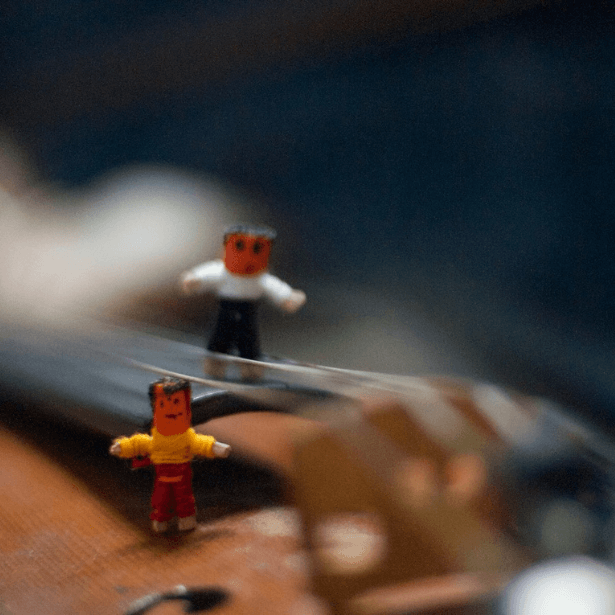Two miniature figures resting on top of a violin, which is slightly blurred out.