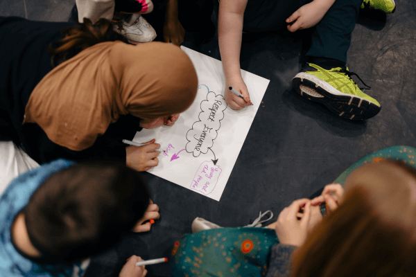 An aerial view of some young children writing down thoughts on a piece of paper.
